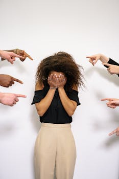 A stressed woman covers her face as multiple hands point accusatorily in a studio setting.