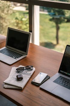 A stylish indoor workspace featuring laptops, smartphone, and accessories on a wooden desk.