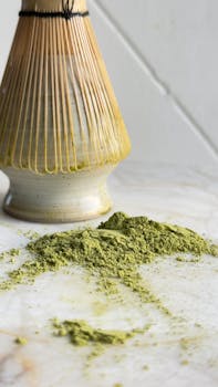 Top view of matcha powder and traditional bamboo whisk on a marble countertop, perfect for tea ceremonies.