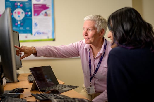 Two women collaborating at a desk in a modern office setting, using technology.