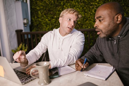 Two men collaborating on a project with a laptop outdoors, discussing ideas.